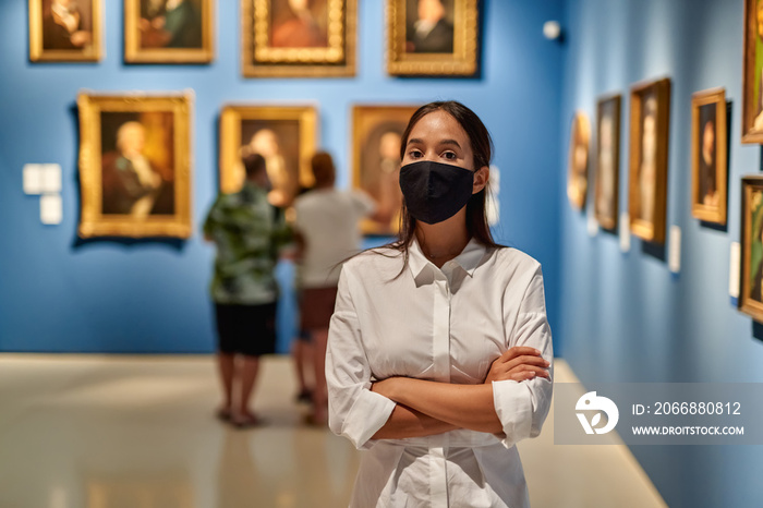 Woman visitor wearing an antivirus mask in the historical museum looking at pictures.