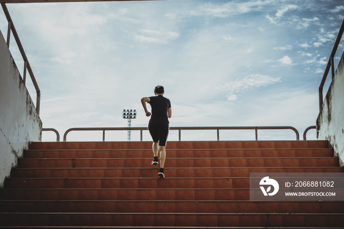 A beautiful woman runner is jogging up the steps under the sunlight. The concept of stepping into success, self-improvement in exercise.