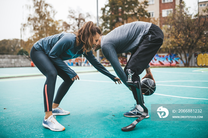 Young man with prosthetic leg playing basketball with his friend.