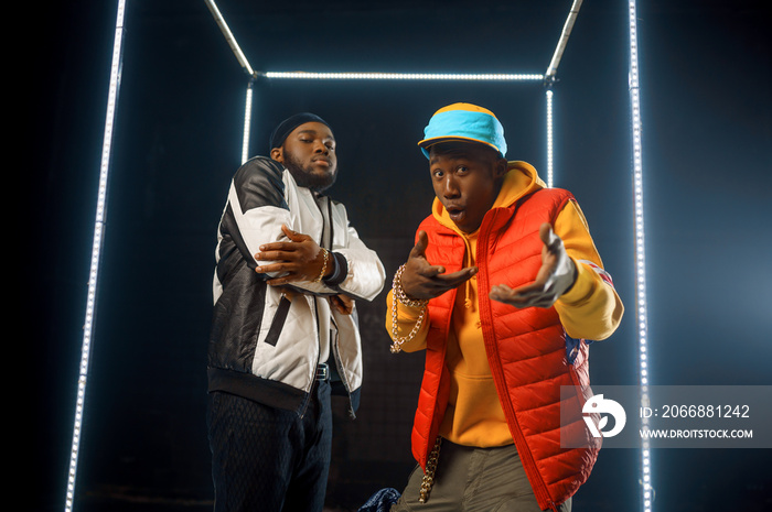 Two stylish rappers poses in glowing cube