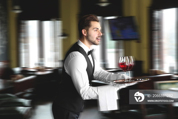 Young hurrying waiter with glasses of wine in restaurant