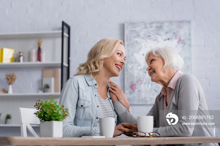 Cheerful women talking near cups and eyeglasses in living room