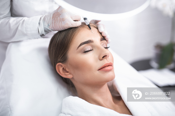 Enjoying the procedure. Close up portrait of smiling young lady with closed eyes. She is getting facial skin lifting treatment at beauty salon