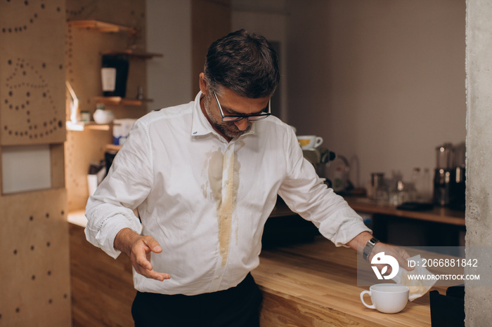 Man is spilling coffee on white shirt while drinking in office..