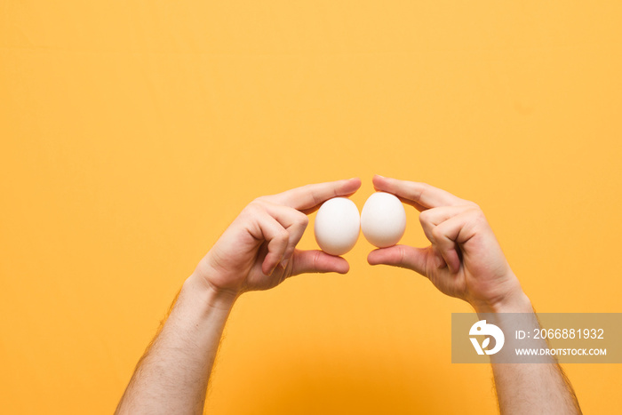 Man holds two eggs in his hand, isolated on a yellow background. Hands with white chicken eggs