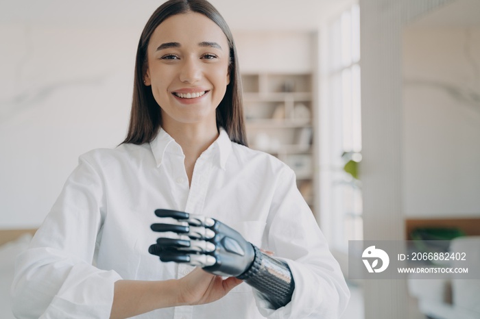 Happy disabled girl enjoy using bionic prosthetic arm, high tech artificial limb, standing at home