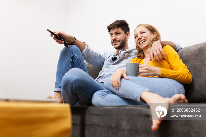 couple in love sitting on a sofa watching tv. holding coffee and remote control