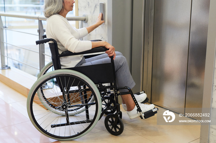 Senior woman sitting in wheelchair and pushing the button she using the elevator in modern building