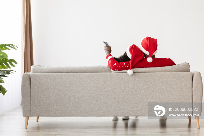 Unrecognizable black couple sitting on sofa at home, holding remote