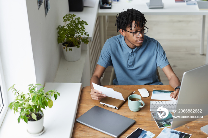 High angle portrait of creative African-American man reviewing photographs while working on editing and publishing in modern office, copy space