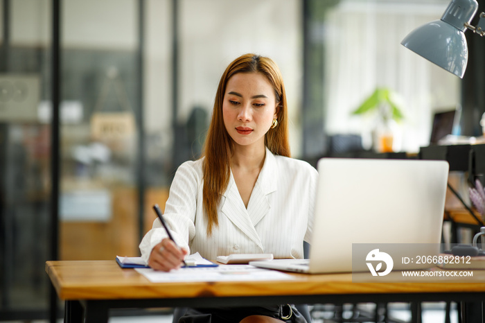 Confident businesswoman documents working on laptop at her workplace at modern office. reading financial report analyzing statistics pointing at pie chart working at her desk.