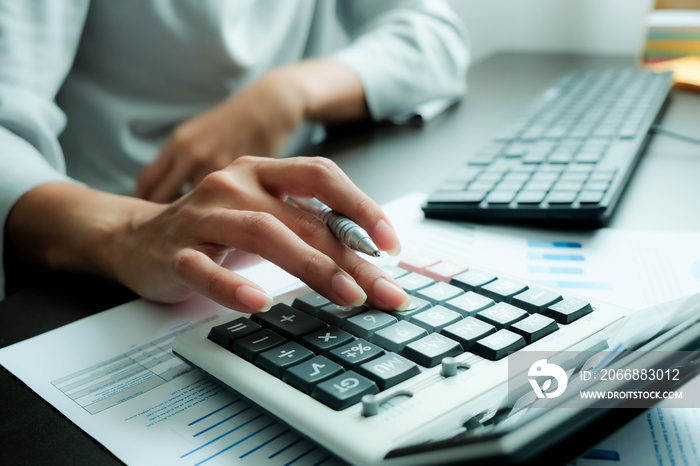 The hand of Asian woman is pressing calculator and prepare information for report to correct. While still holding a silver pen in finger. When calculated completed, can be recorded immediately.