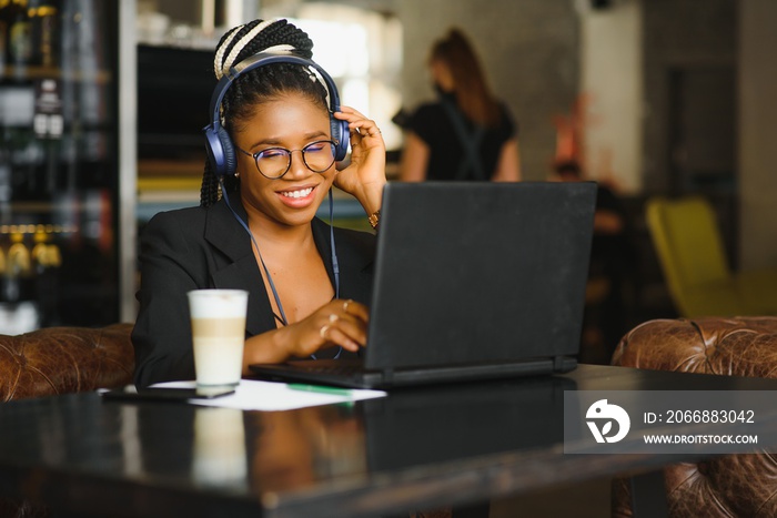 Attractive African American blogger with headphones and laptop communicating with followers in cafe