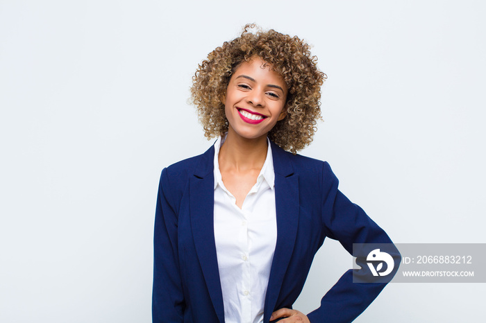 young woman african american smiling happily with a hand on hip and confident, positive, proud and friendly attitude against flat wall