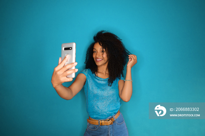 Social media influencer streaming video with her smartphone. Afro hairstyle black touching taking selfie.