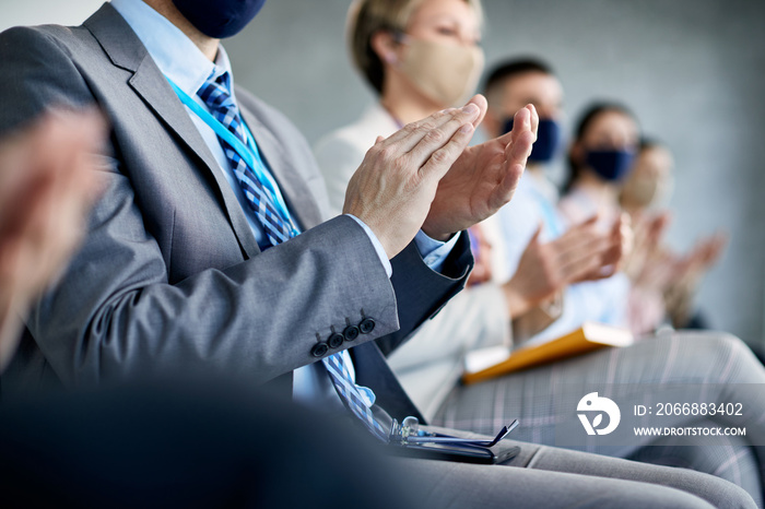 Close-up of entrepreneur and his colleagues applauding after successful business presentation during COVID-19 pandemic.