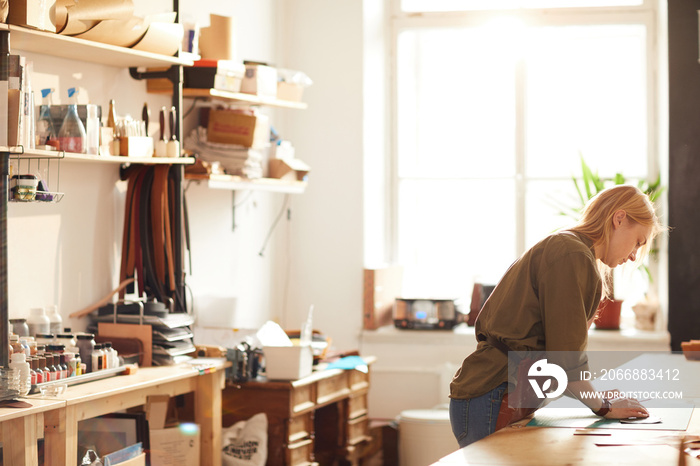 Side view portrait of young woman working in artisan workshop lit by sunlight, copy space