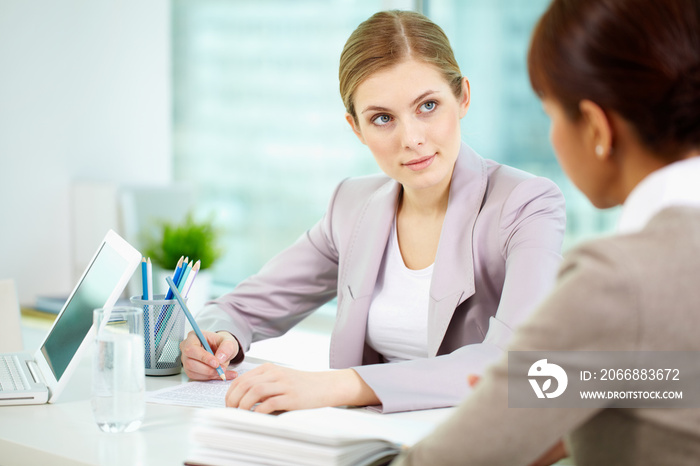 Serious businesswoman listening to woman and writing something