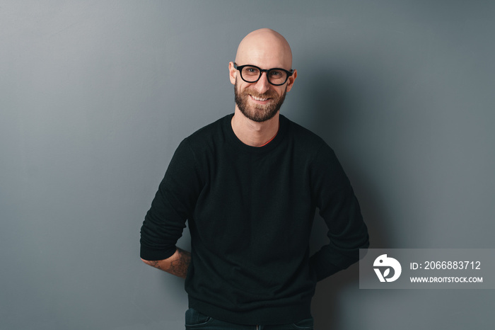 Young smiling man with beard and glasses on gray studio background