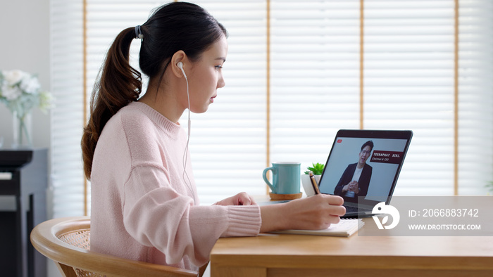 Back rear view young asian woman listen to virtual business conference webinar, management town hall or all hands meeting at home in quarantine social distance work remotely with asia speaker concept.