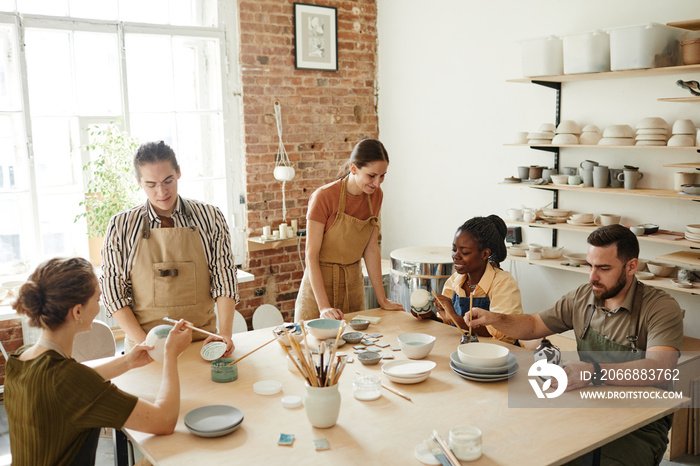 Warm toned shot of creative group of people decorating ceramics in pottery workshop, copy space