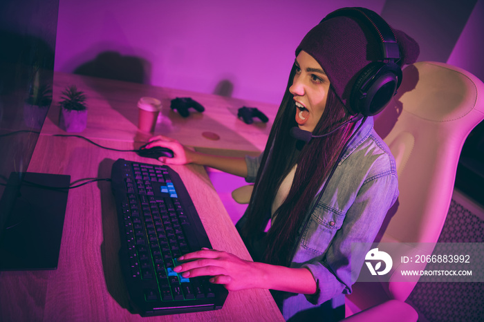 Photo of interested focused thoughtful emotional girl wearing jeans denim washed with pink neon violet purple lights sitting in computer club