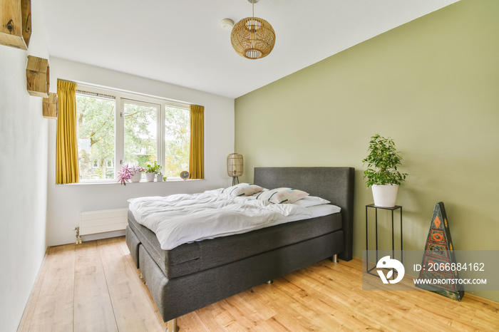 a bedroom with a bed, lamp and plants in the window simng it’s bright green walls