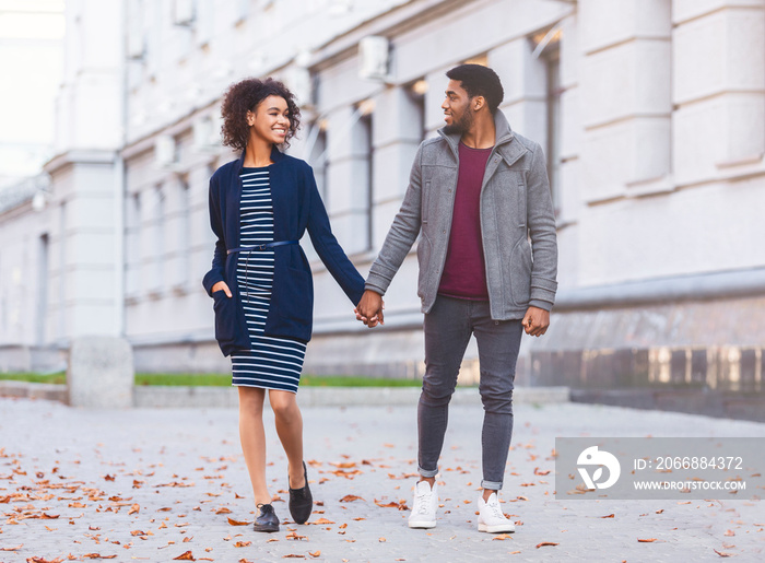 Millennial lovers walking by street, holding hands