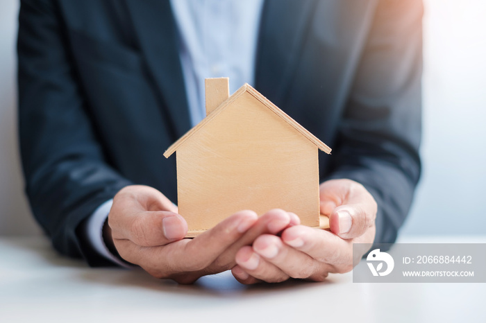 Businessman hand holding wooden Home model. Real estate, buy and sale, Property insurance, rental and contract agreement concepts