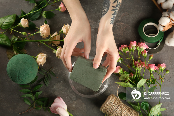 Female florist using sponge for work on grey background