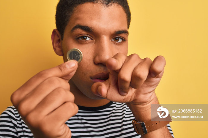 Young handsome arab man holding euro coin standing over isolated yellow background pointing with finger to the camera and to you, hand sign, positive and confident gesture from the front