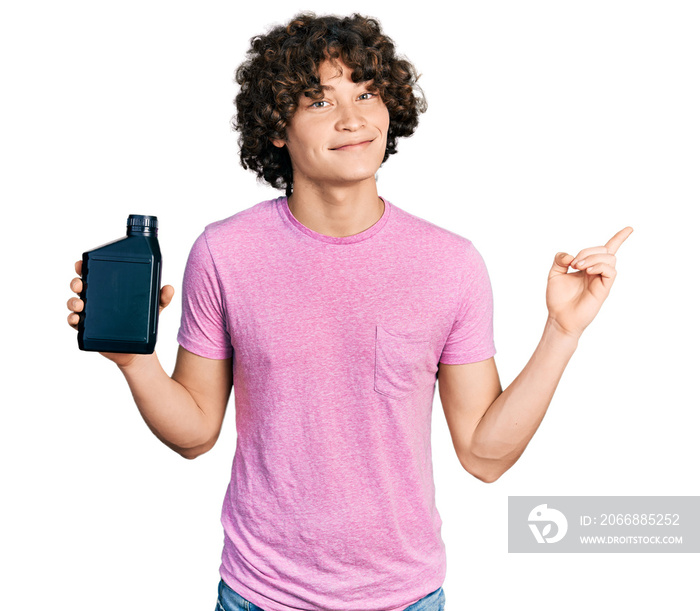 Caucasian teenager holding motor oil bottle smiling happy pointing with hand and finger to the side