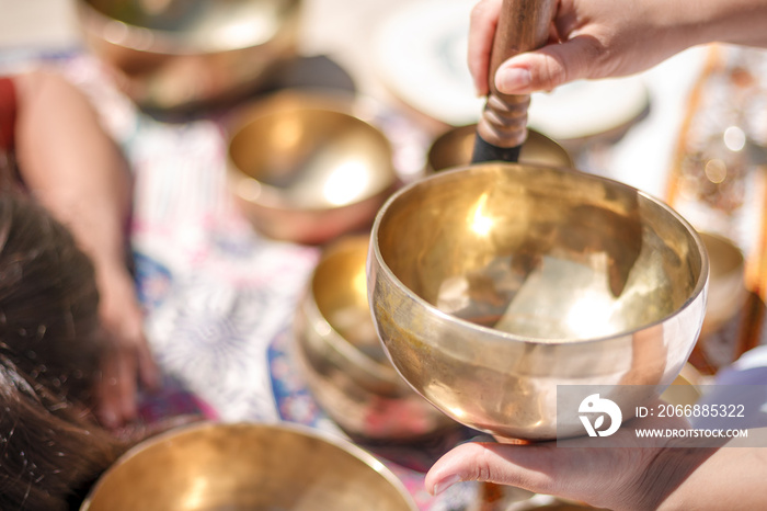 Woman playing a singing bowls also known as Tibetan Singing Bowls, Himalayan bowls. Making sound massage at beautiful sunny day.