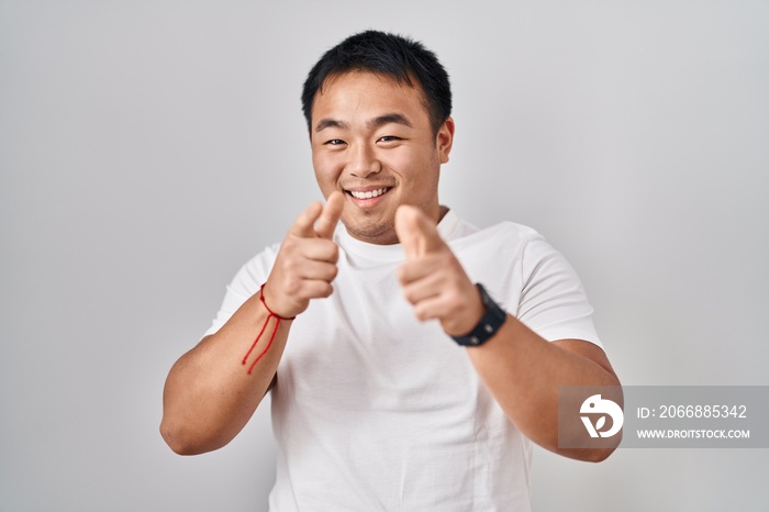 Young chinese man standing over white background pointing fingers to camera with happy and funny face. good energy and vibes.