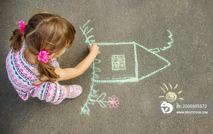 The child draws the house with chalk on the asphalt. Selective focus.