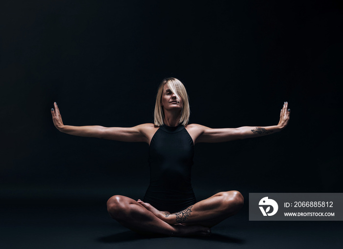 a forty-year-old woman in excellent physical shape with elastic muscles and healthy skin performs yoga exercises on a dark background. Studio photography. excellent health at forty.