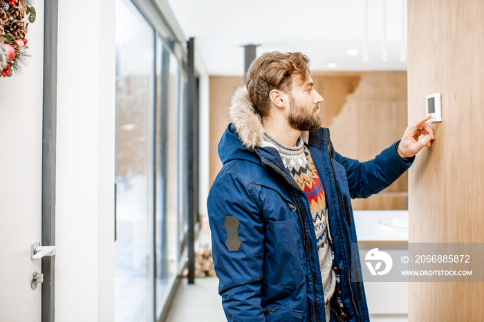 Man in winter clothes feeling cold adjusting room temperature with electronic thermostat at home