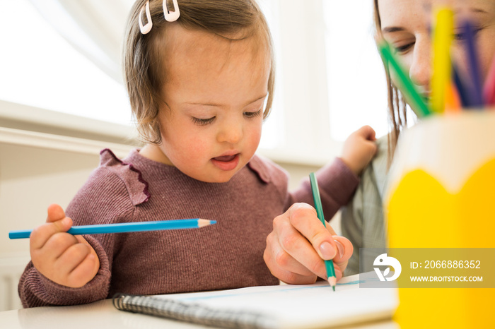 Girl with down syndrome drawing and sitting over sheet of paper at the table