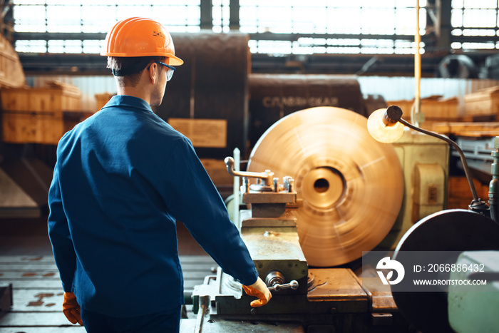 Turner in uniform and helmet works on lathe