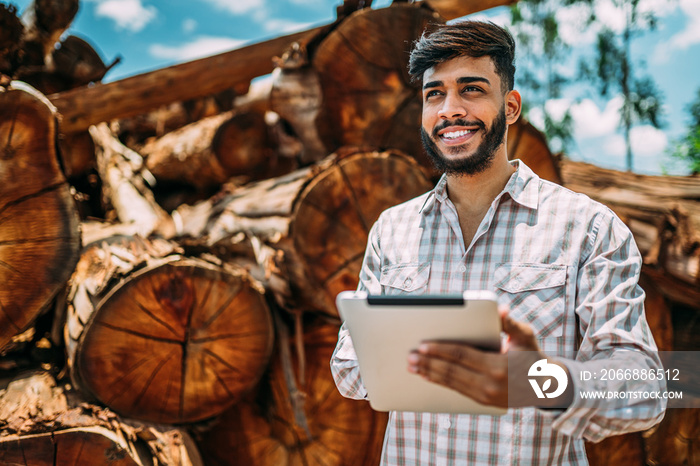 Portrait of Latin young man working on tablet beside tree trunks.