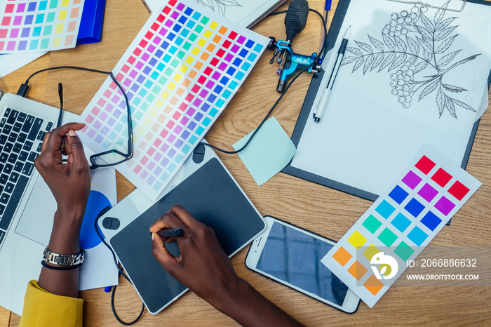 hands of afro american woman in a stylish yellow jacket and multi-colored dreadlocks pigtails is graphic designer draws a sketch on a tablet in workplace in a light large modern office