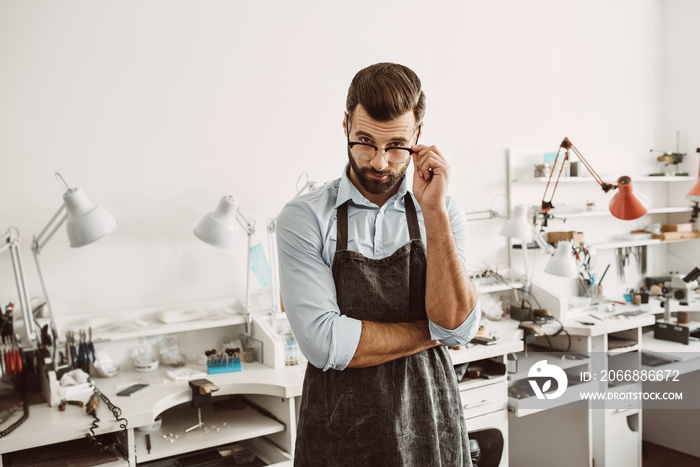 Professional of his business. Portrait of confident male jeweler wearing apron and adjusting glasses