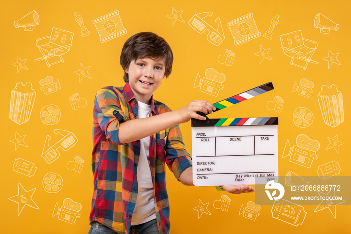 Future blockbuster. Jolly energetic boy carrying clapperboard and looking at camera