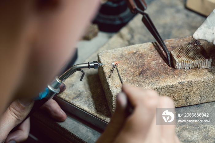 Diligent jeweler working on a chain heating up some links