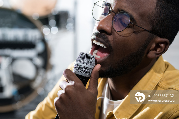 Head and shoulders portrait of inspired African-American man singing to microphone while performing on stage, copy space