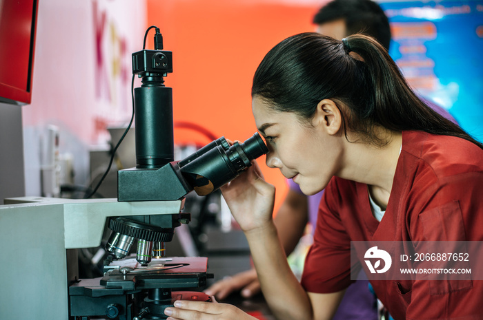 Asian young female farmer looking through a microscope in a laboratory. Modern technologies in agriculture management, agribusiness and research concept.