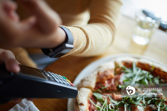 Smartwatch on human hand over payment machine in process of contactless paying in modern cafe