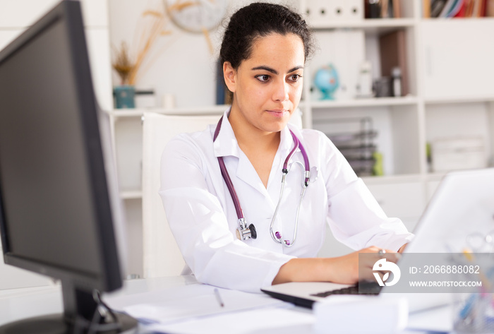 Portrait of female doctor who is working with laptop and documents