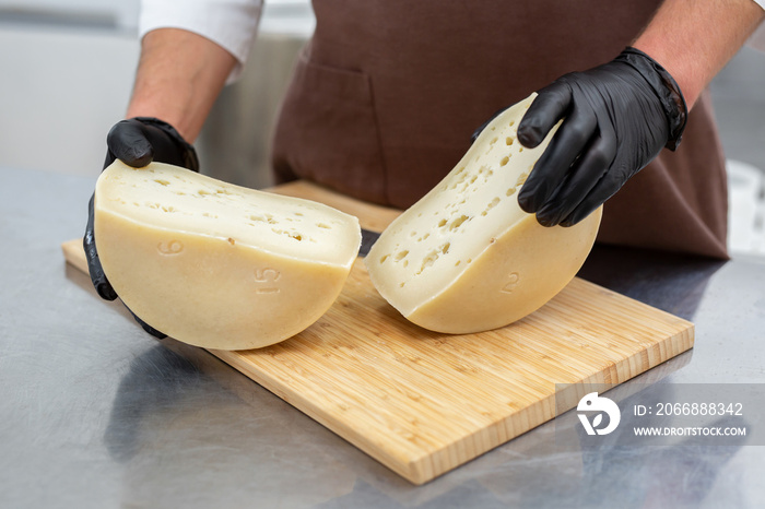 Cheese maker cuts a cheese head with a knife on a wooden board at a private cheese factory.