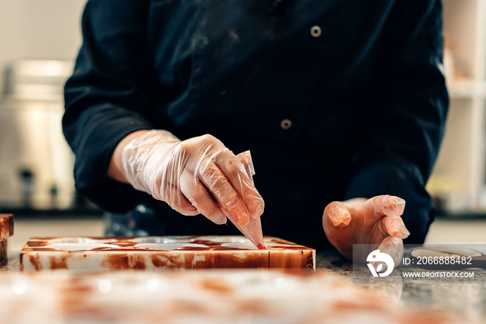 close up on hands of a pastry chef decorating white chocolates in an artisanal workshop